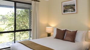 A neatly made bed with a brown throw blanket, two bedside lamps, and a framed landscape painting on the wall. - Twin Tree Bush Cabin in the Heart of the Hunter Valley! 
1 of 10 Cabins listed! (Pokolbin)