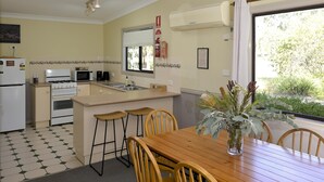 A modern kitchen with a dining area, featuring a central island, bar stools, and a wooden table with chairs. - Twin Tree Bush Cabin in the Heart of the Hunter Valley! 
1 of 10 Cabins listed! (Pokolbin)