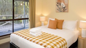 A hotel room with a large bed, two bedside lamps, a checkered bedspread, and a painting on the wall.