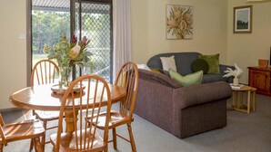 A dining area with a wooden table and chairs, a sofa with cushions, and a small side table with a vase.