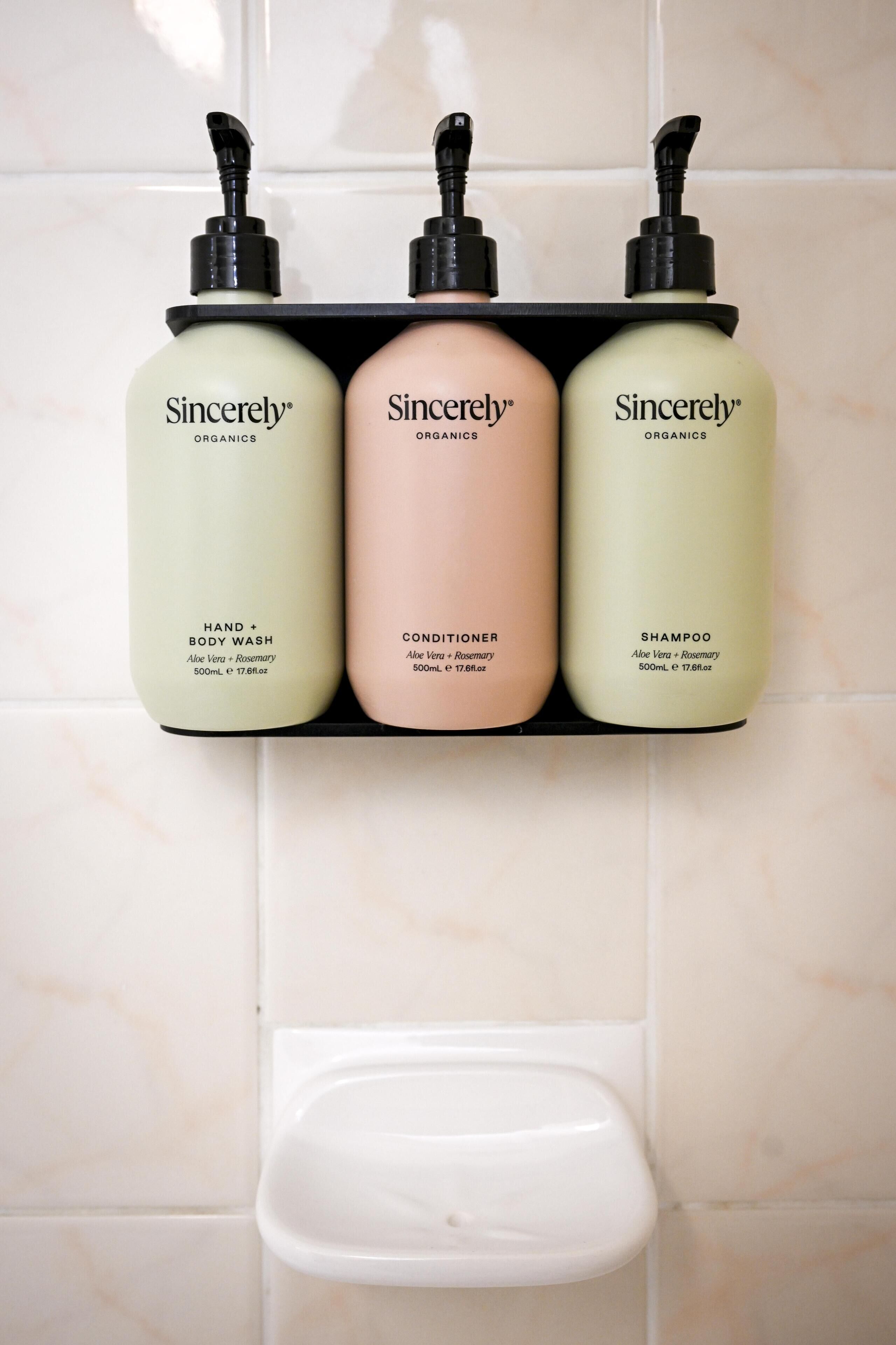 Un estante de baño con tres productos de Sincerely Organics: jabón de manos y cuerpo, acondicionador y champú.