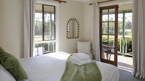 A hotel room with a large bed, a ceiling fan, a view of the outdoors, and a balcony with a table and chairs.