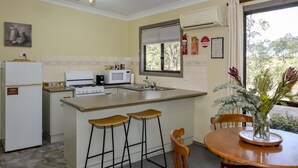 Cocina compacta con isla central, taburetes de bar, mesa de comedor y vista a zonas verdes.