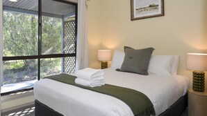 A neatly made bed with white linens and a green throw, two bedside lamps, and a framed picture on the wall. - Greyvillea Bush Cabin in the Heart of the Hunter Valley! 
1 of 10 Cabins listed! (Pokolbin)
