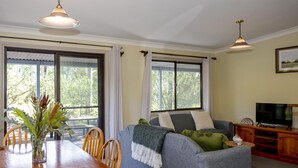 A living room with a sofa, television, and a dining table with chairs. - Greyvillea Bush Cabin in the Heart of the Hunter Valley! 
1 of 10 Cabins listed! (Pokolbin)
