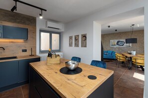 A modern kitchen with a wooden island, built-in appliances, and a dining area with yellow chairs and a blue sofa. -  Casa Giuseppe (Labin)