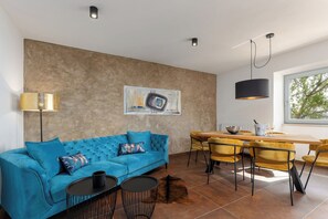A modern living room with a blue sofa, a dining table with yellow chairs, a painting on the wall, and a large window. -  Casa Giuseppe (Labin)
