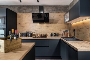 A modern kitchen with a wooden countertop, black cabinets, a built-in microwave, and a range hood. - Casa Giuseppe (Labin)
