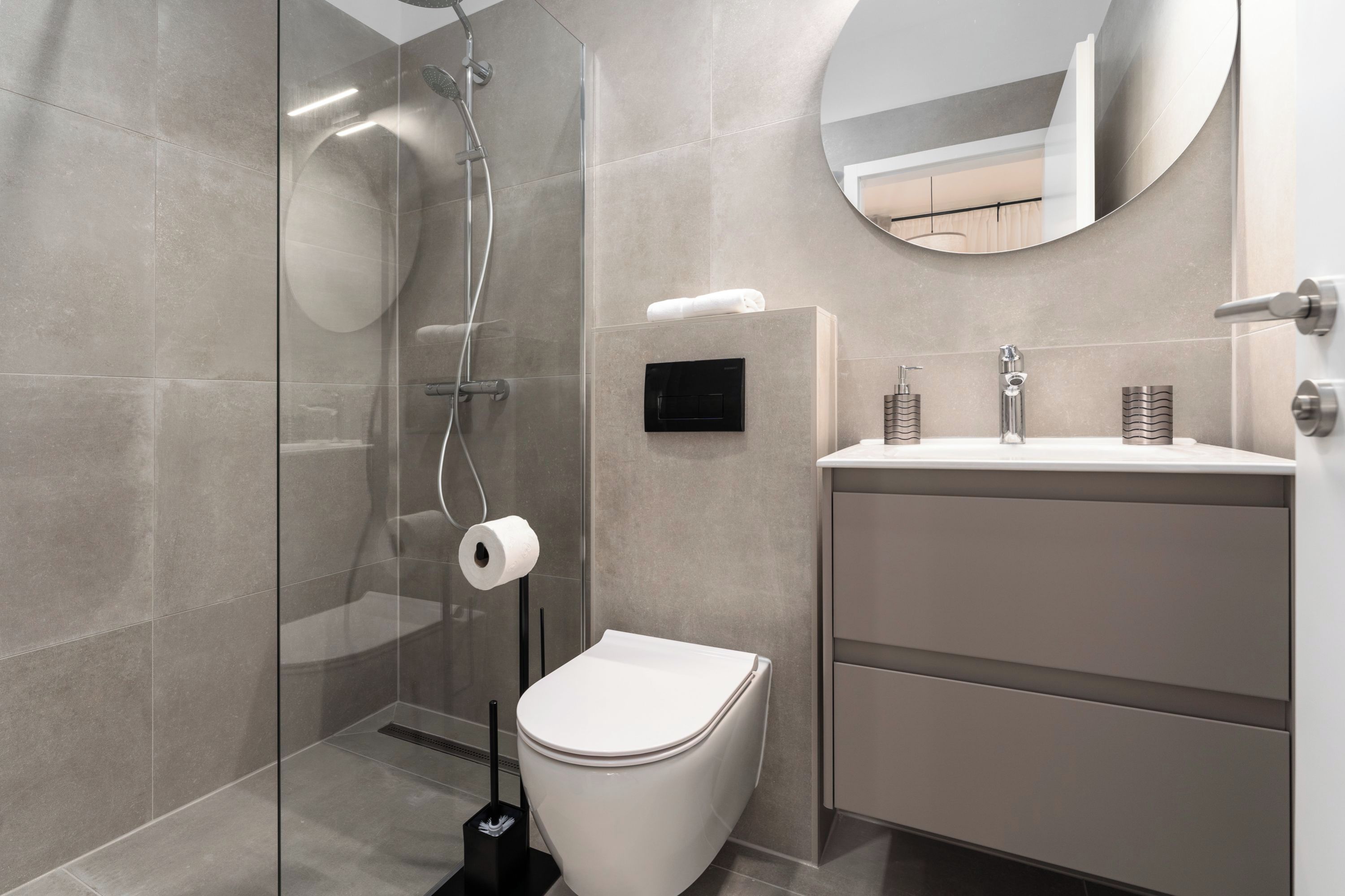 Een moderne badkamer met een douchecabine van glas, een toilet, een wastafel met spiegel en een handdoekhouder.