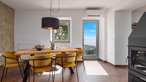 A modern dining area with a wooden table and yellow chairs, a black pendant light, and a view through a window. -  Casa Giuseppe (Labin)
