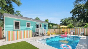 Ein Garten mit Schwimmbad, einem kleinen Haus und einem farbenfrohen Zaun.