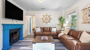 Ein Wohnzimmer mit Fernseher, Kamin in Blau, braunes Ledersofa, Couchtisch und einer Schiffslenken-Dekoration.