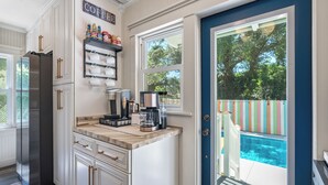 Eine Küche mit weißen Schränken, einem Edelstahl-Kühlschrank, einer Kaffeestation und Blick auf einen Gartenpool.