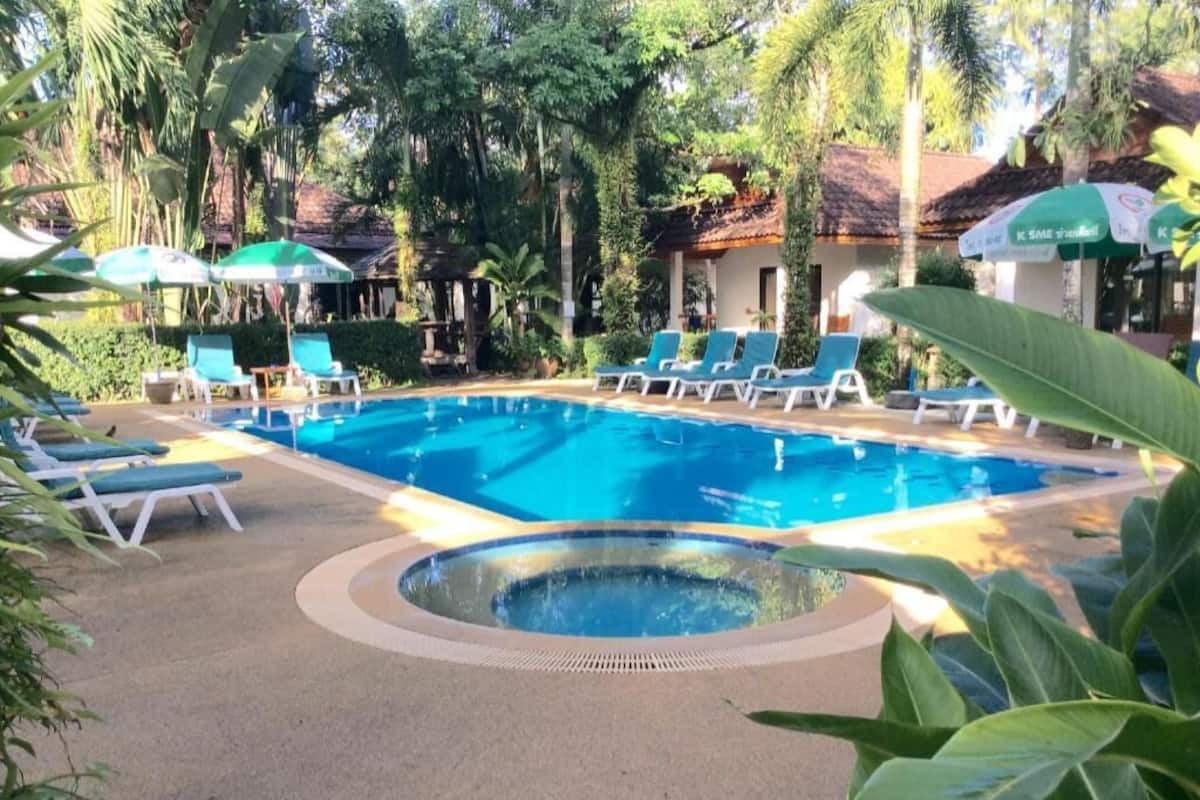Piscina com espreguiçadeiras e guarda-sóis, cercada por vegetação.