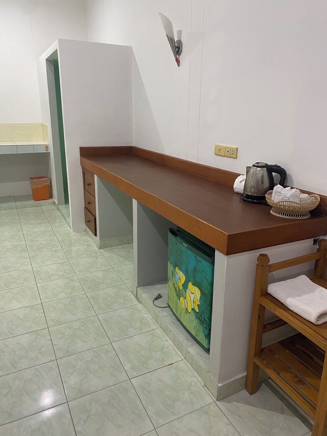 A kitchen with a wooden countertop, a kettle, a basket, and a trash bin.