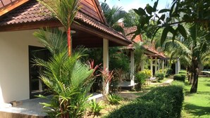 Un resort con un espacio exterior techado, palmeras y un césped bien cuidado.