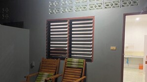 Una habitación con dos sillas de madera, una mesita, una ventana con persianas y un panel decorativo en la pared.