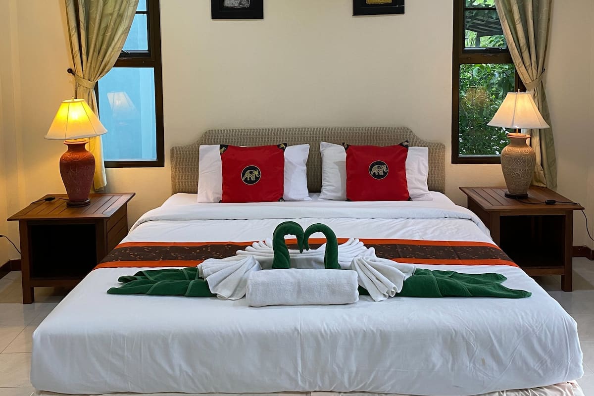 Quarto de hotel com uma cama grande, duas mesas de cabeceira, duas luminárias, uma janela com cortinas e duas obras de arte emolduradas na parede.