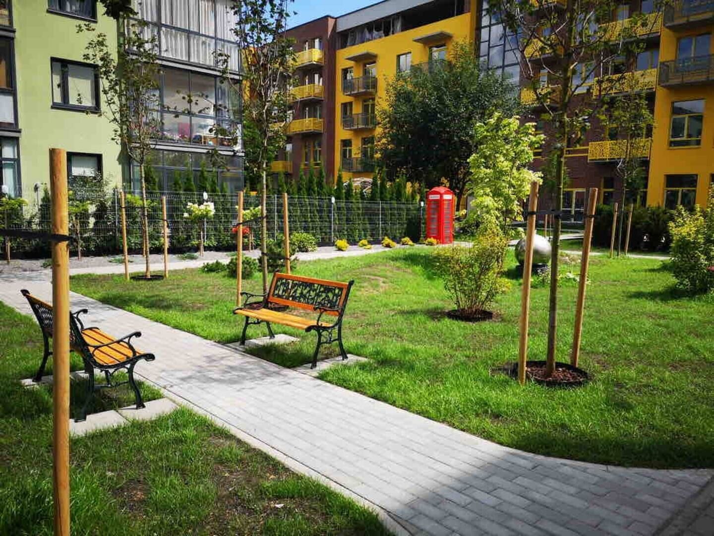Une cour avec un banc, un sentier et une cabine téléphonique rouge.