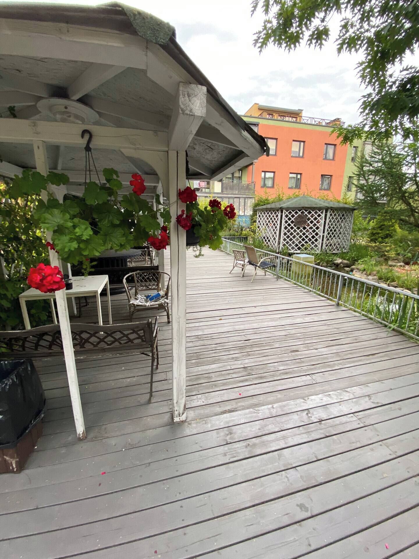 A wooden deck with a covered seating area, a grill, and a view of a multi-story building in the background.