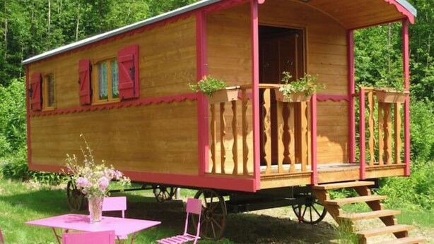 A wooden carriage-style cabin with a porch and steps, surrounded by greenery. - Roulotte Cévenole (Aulas)