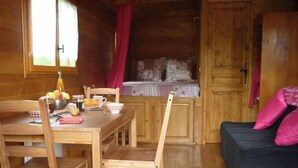 A wooden cabin interior with a dining table, chairs, a small kitchenette, and a sofa. - Roulotte Cévenole (Aulas)
