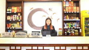 A reception desk with a woman behind it, surrounded by shelves of products and a large abstract painting. - Meishike Express Hotel (Emeishan City)