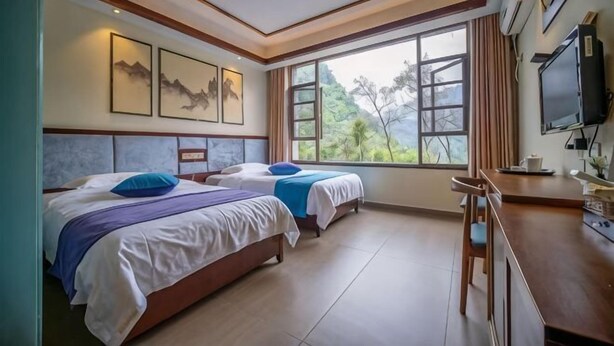 A hotel room with two beds, a TV, and a window with a view of trees. - Meishike Express Hotel (Emeishan City)