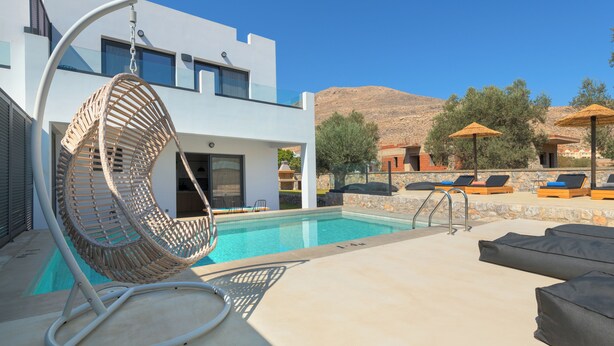 Zona de piscina exterior moderna con una silla colgante, sillas de descanso y vistas a la montaña.