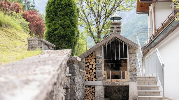 A stone fireplace with stacked firewood, a stone bench, and a staircase leading to a wooden deck.