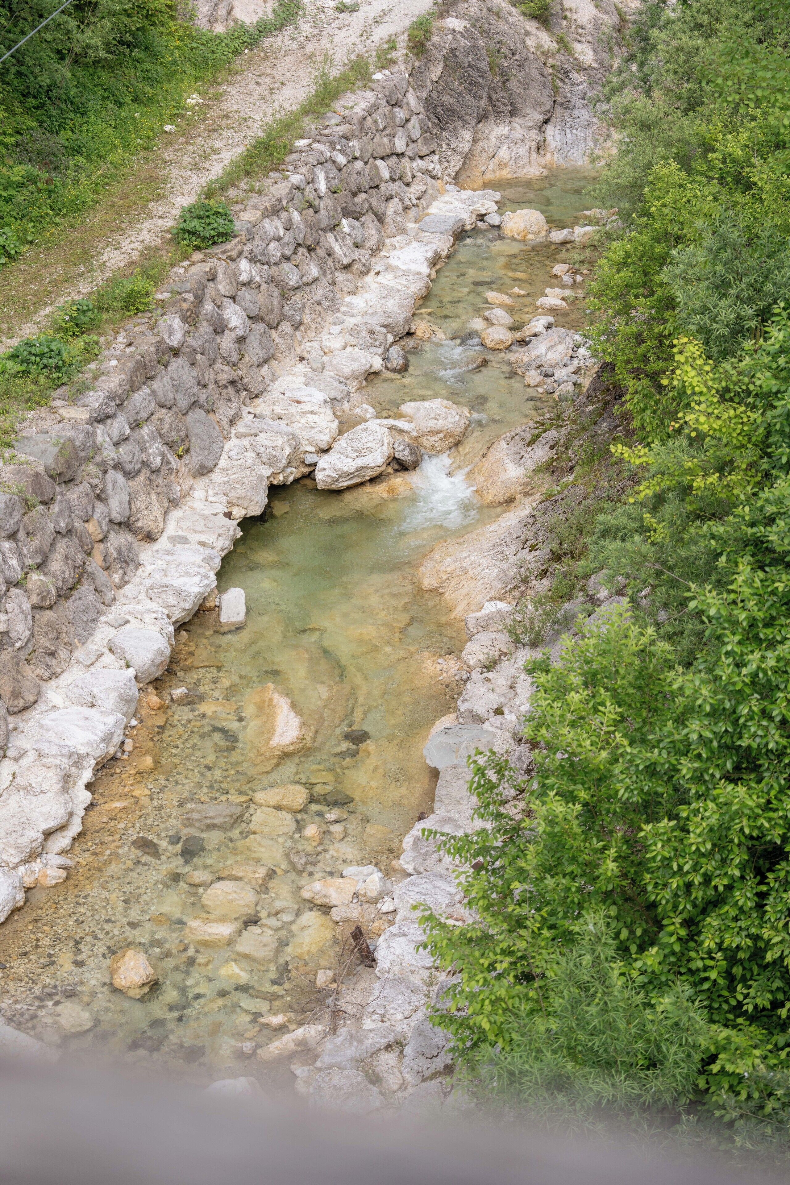 Un ruisseau naturel bordé d’un muret de pierres, entouré de verdure.