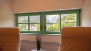A room with a view of a mountainous landscape through a green-framed window.