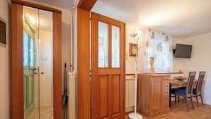 A room with a wooden door, a radiator, a dining table with chairs, and a television mounted on the wall. - Cosy apartment for 2 persons in mountain area (Log pod Mangrtom)