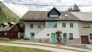 A two-story house with green doors and windows, a sloped roof, and a small balcony. - Cosy apartment for 2 persons in mountain area (Log pod Mangrtom)