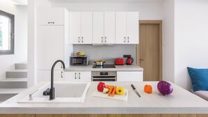 A modern kitchen with white cabinets, a black faucet, a microwave, a red toaster, and a cutting board with vegetables.