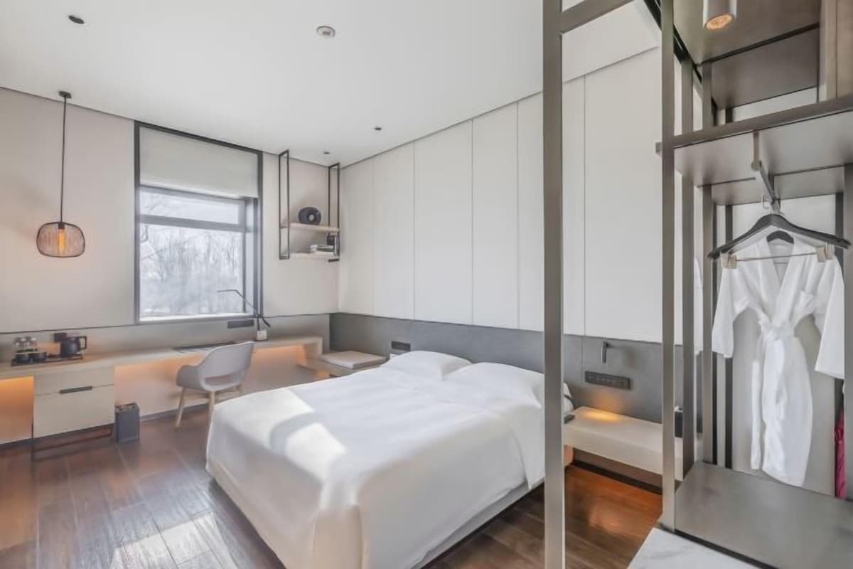 Una habitación de hotel moderna con una cama grande, un escritorio, una silla y un armario.