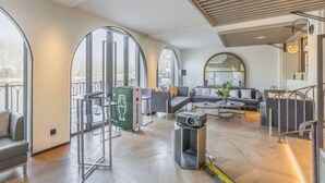 A modern living room with a sofa set, a coffee table, and a television. There is a large window with a view of the city. - Xiongan Kapok Hotel (Xiong County)