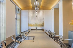 Un salón de conferencias con una larga mesa, sillas, una araña y un cuadro abstracto grande en la pared.