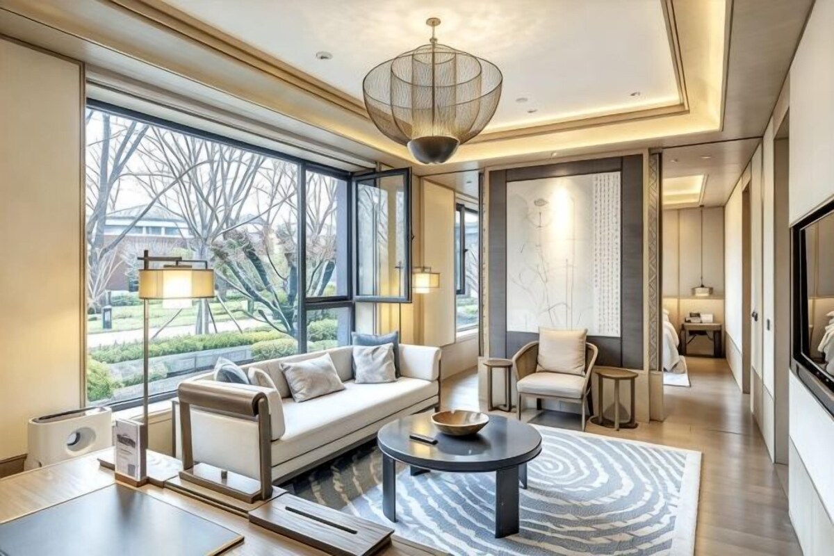 Quarto de hotel moderno com uma grande janela, um sofá, uma mesa de centro e um candelabro.