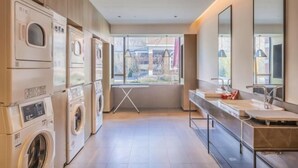 A modern laundry room with multiple washing machines, a drying rack, and a long counter with sinks and mirrors. - Xiongan Kapok Hotel (Xiong County)