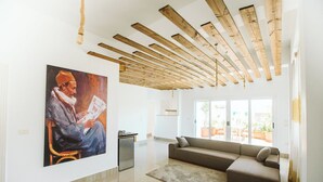 A spacious living area with a wooden ceiling, a large painting on the wall, a sofa, and a kitchen in the background. - Arabian Nights - Modern Duplex Villa (6th of October City)