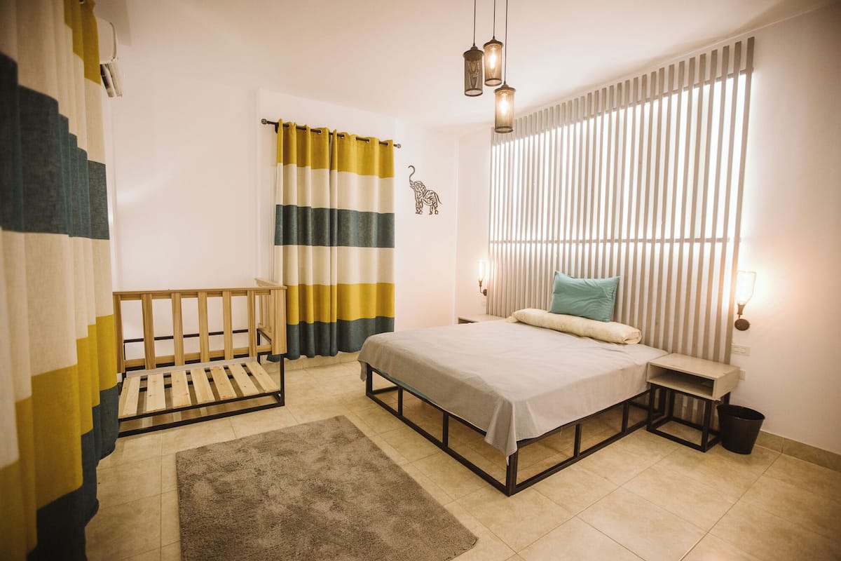 A bedroom with a bed, bedside table, and a window with blinds.