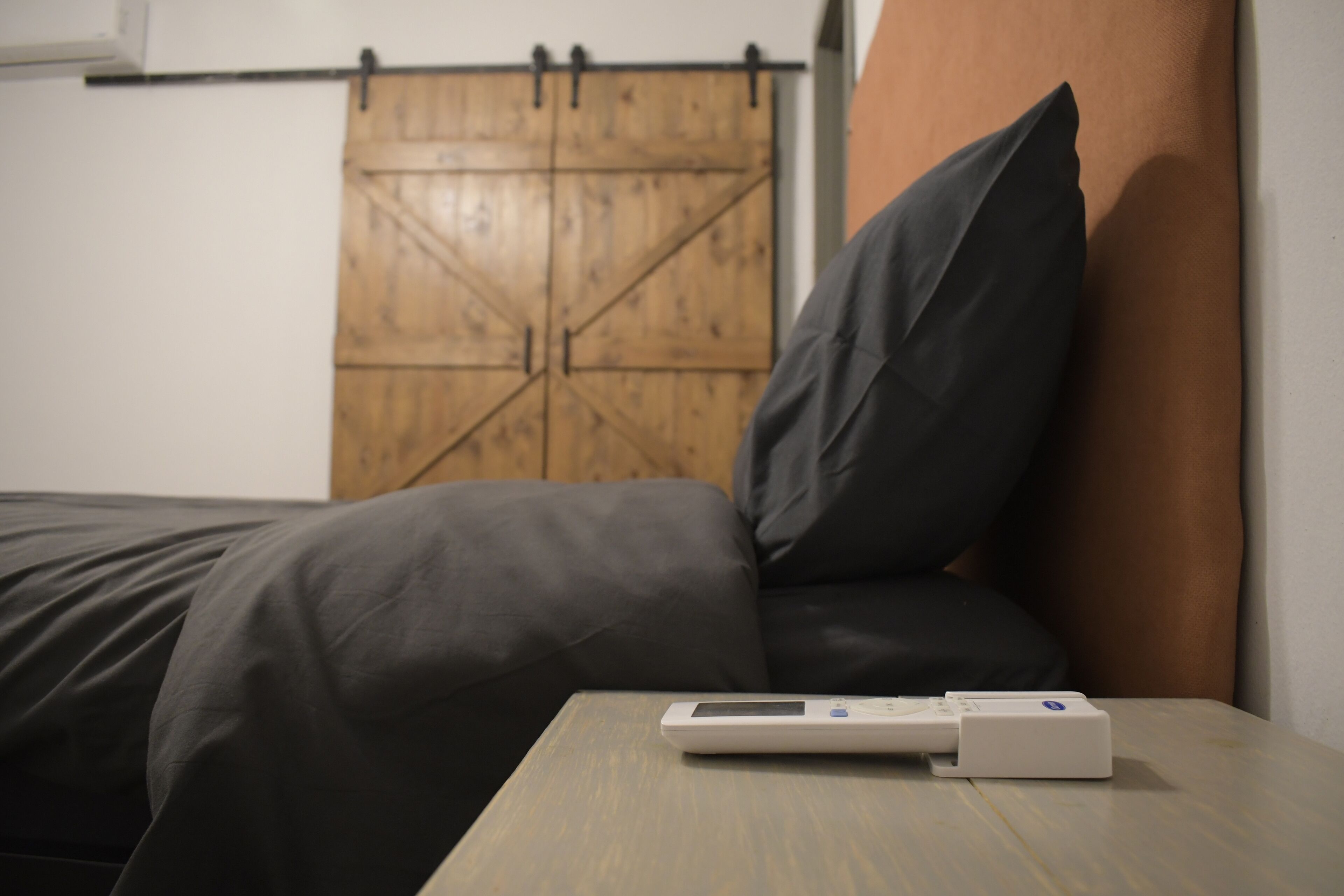 A bed with a dark gray mattress and a white bedside table with a digital device on it.