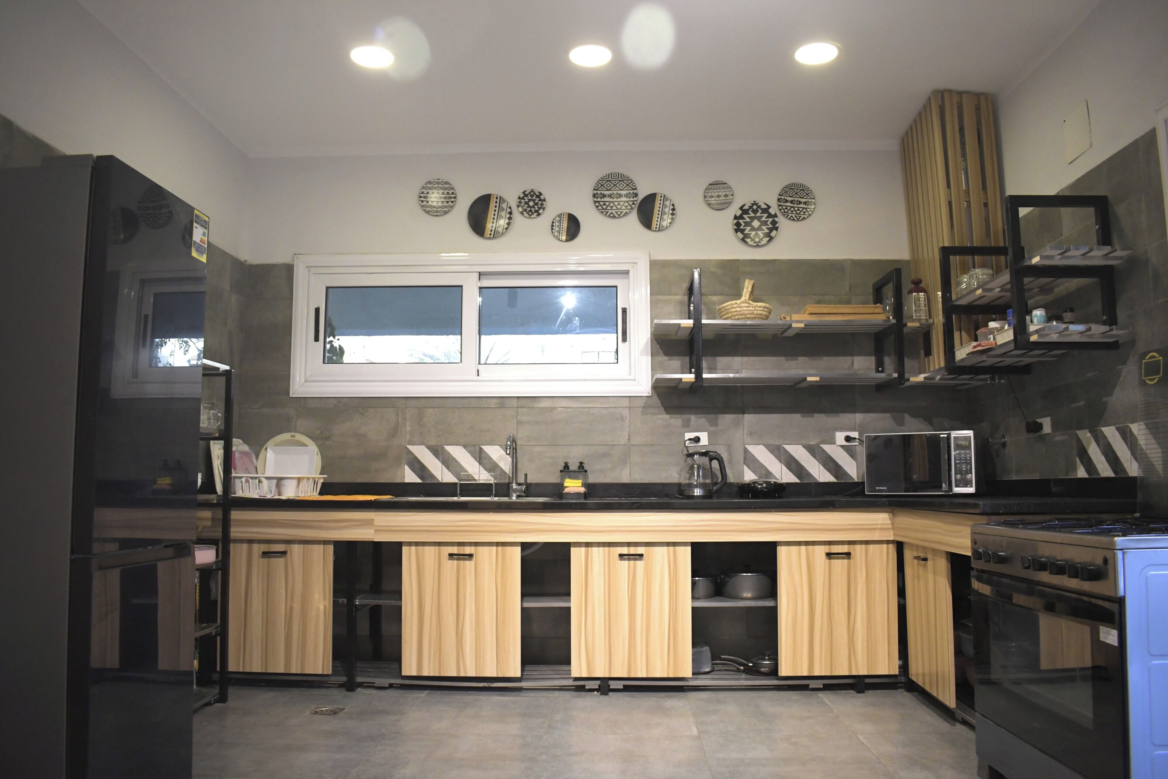 A modern kitchen with wooden cabinets, a black countertop, a microwave, a stove, and decorative plates on the wall.
