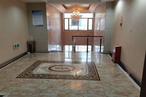 Un hall d’hôtel avec un tapis à motifs, un lustre, un comptoir d’accueil et une vue sur l’extérieur grâce à de grandes fenêtres.