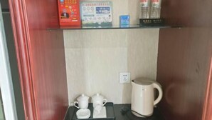 A hotel room with a shelf containing a red box, a blue box, and two bottles of water. There is a tray with two white cups and a teapot on the table. - Changshou Business Hotel (Luntai)