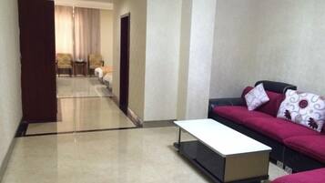 A hotel room with a sofa, a small table, a door, and a view into another room.