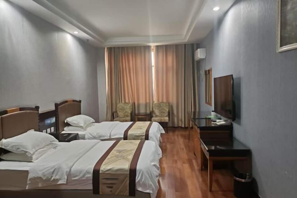 Une chambre d’hôtel avec deux lits, un bureau, une chaise, une télévision et une fenêtre avec des rideaux.