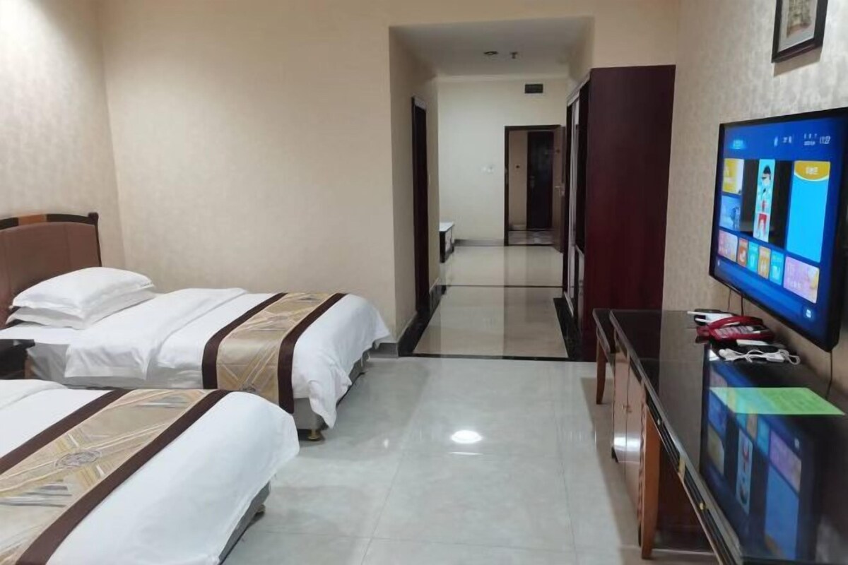 A hotel room with two beds, a flat-screen TV, and a desk with a computer.