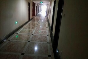 Un long couloir étroit, avec un sol à carreaux, des portes de chaque côté et des panneaux indiquant les sorties de secours.
